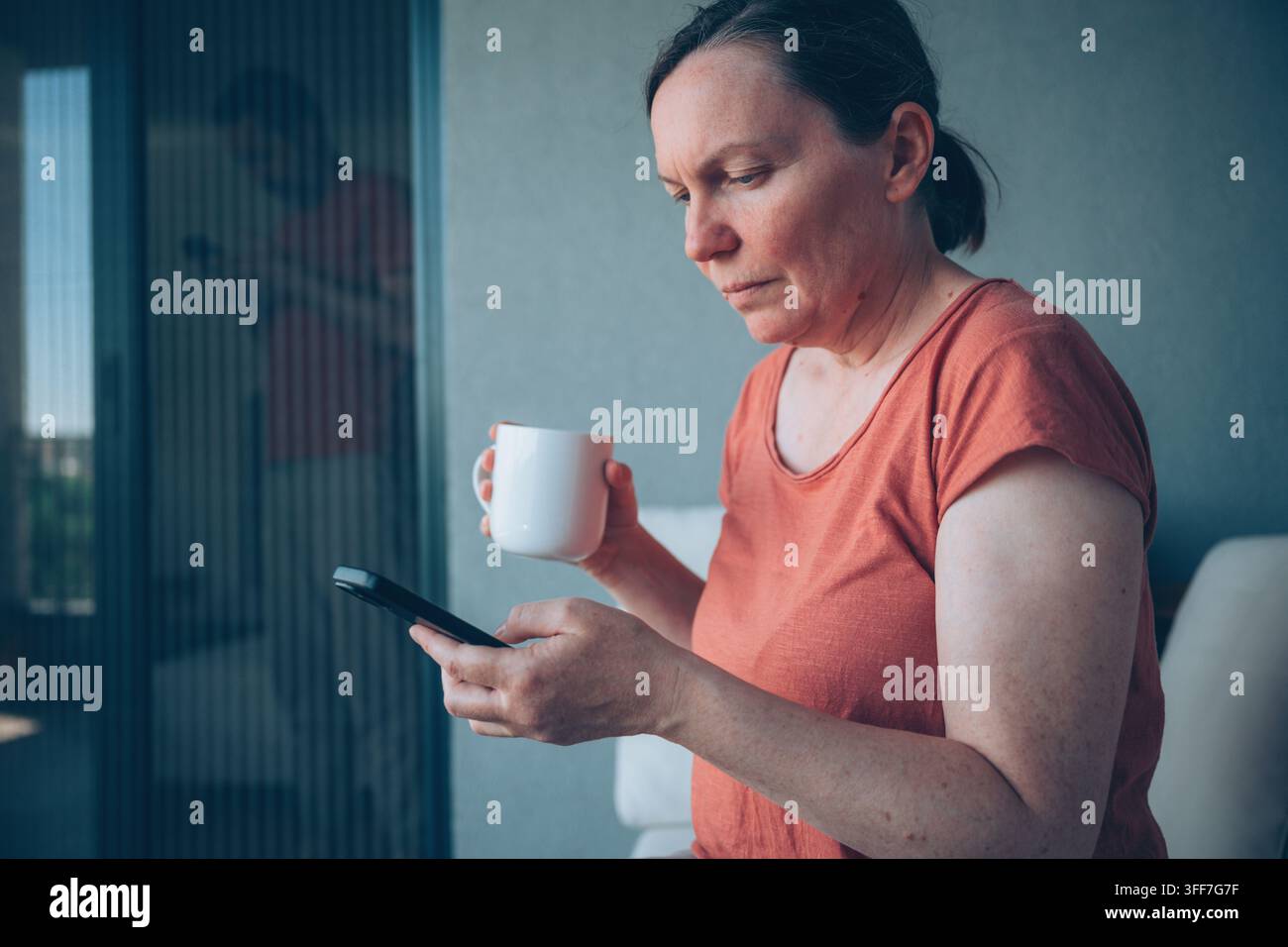 Femme assise avec un café et un smartphone tandis qu'un homme vérifie son téléphone en arrière-plan, thème de la distance émotionnelle, mise au point sélective Banque D'Images