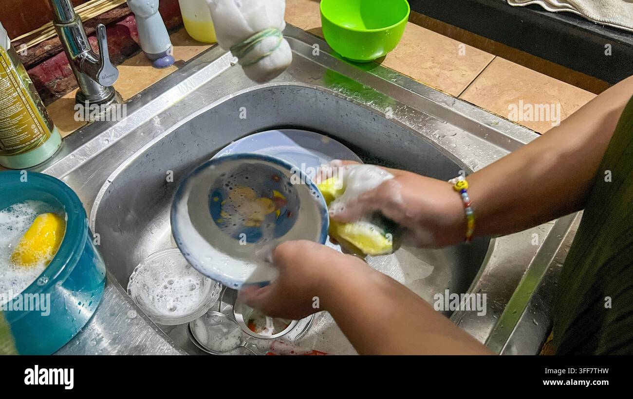 Femme lavant la vaisselle sale à la main avec du savon, représentant le nettoyage de la cuisine, les tâches ménagères, l'hygiène et l'activité domestique quotidienne. Banque D'Images