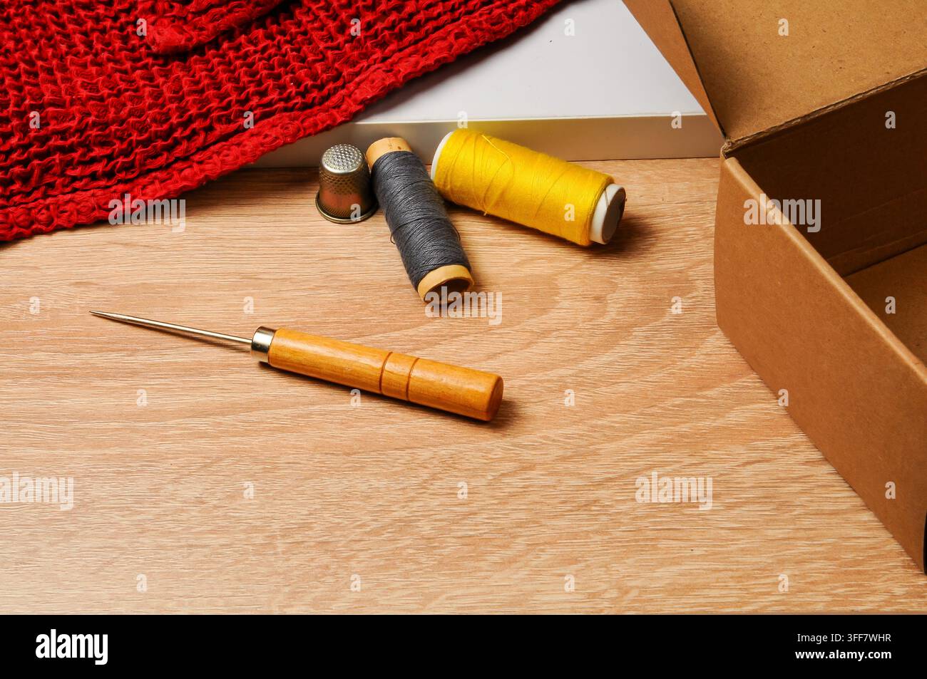 Une collection d'outils et de matériaux de couture est disposée sur une surface en bois clair, suggérant un projet de bricolage ou de réparation en cours Banque D'Images