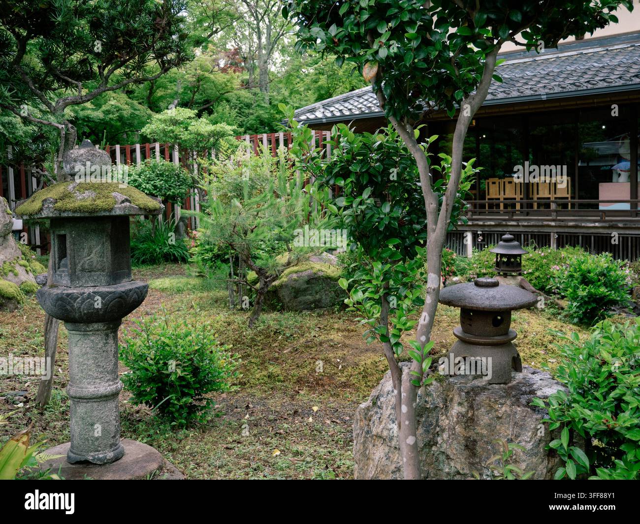 Lanternes en pierre dans un jardin japonais traditionnel avec une végétation luxuriante et un bâtiment en bois, arrondissement d’Ukyo, Kyoto, Japon Banque D'Images