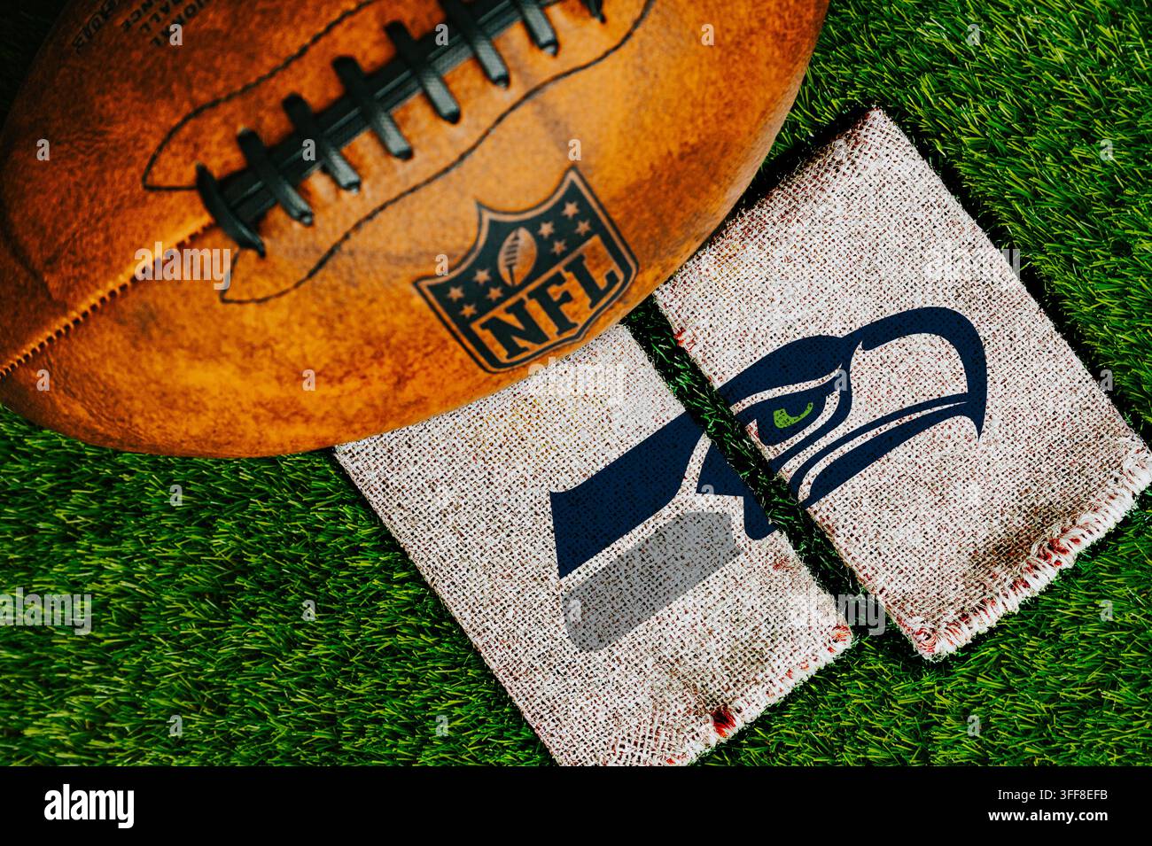 WASHINGTON, ÉTATS-UNIS, 7 SEPTEMBRE 2026 : Logo de l'équipe des Seattle Seahawks imprimé sur un tissu de jute rustique à côté d'un ballon de football en cuir officiel de la NFL sur une pelouse verte. Banque D'Images