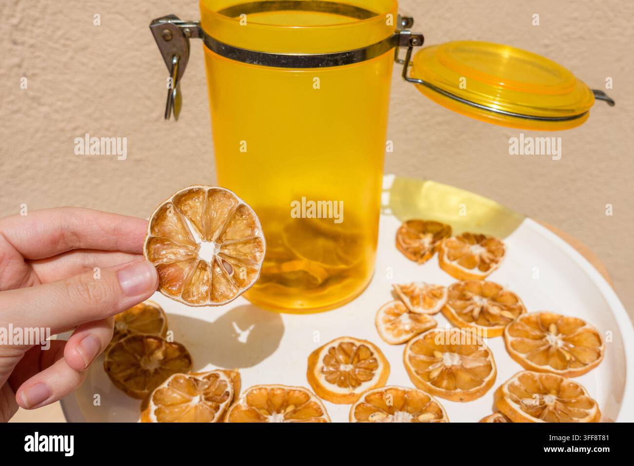 Main tenant une tranche de citron séchée avec un bocal et une assiette de citrons séchés Banque D'Images