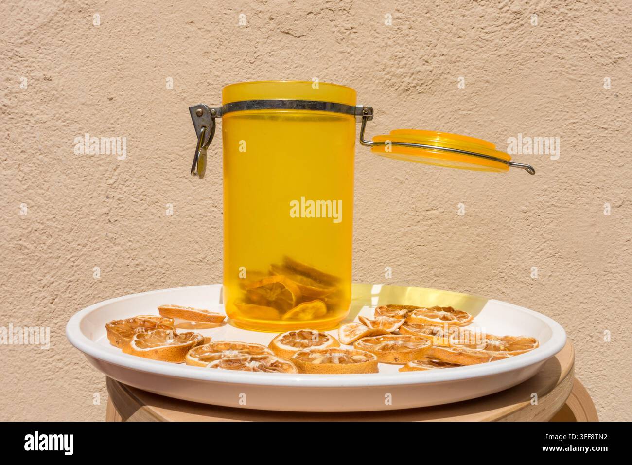 Tranches de citron séchées avec pot jaune et assiette blanche sur un fond crème neutre Banque D'Images