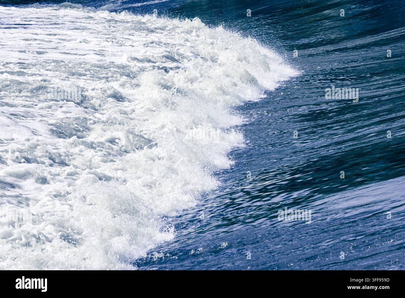 Un cliché d'action dynamique d'une vague de fleuve froide et puissante se brisant sur un barrage structuré, créant un motif épuré d'eau bleu profond et de tourbillons blancs Banque D'Images