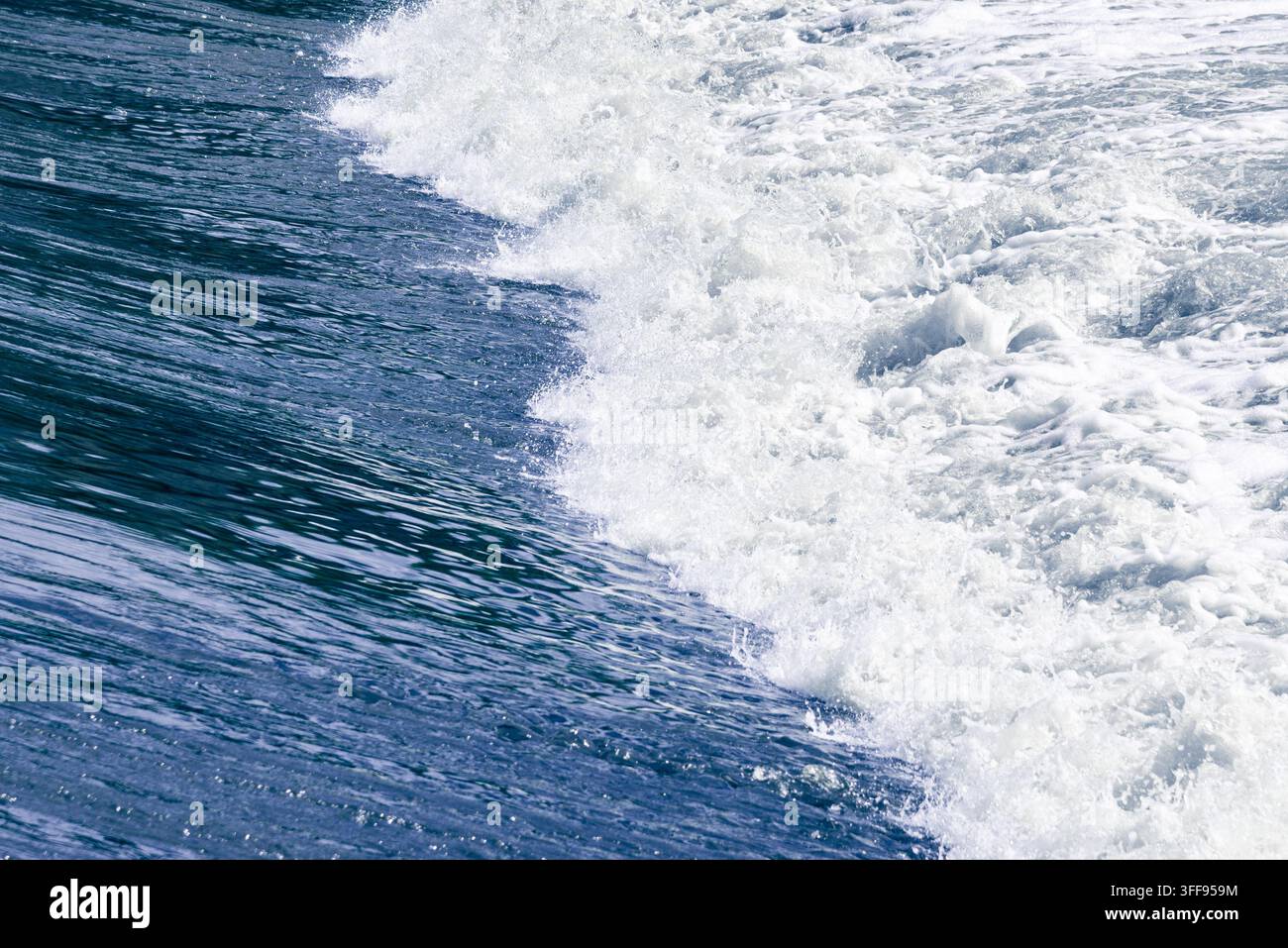 Un cliché d'action dynamique d'une vague de fleuve froide et puissante se brisant sur un barrage structuré, créant un motif épuré d'eau bleu profond et de tourbillons blancs Banque D'Images