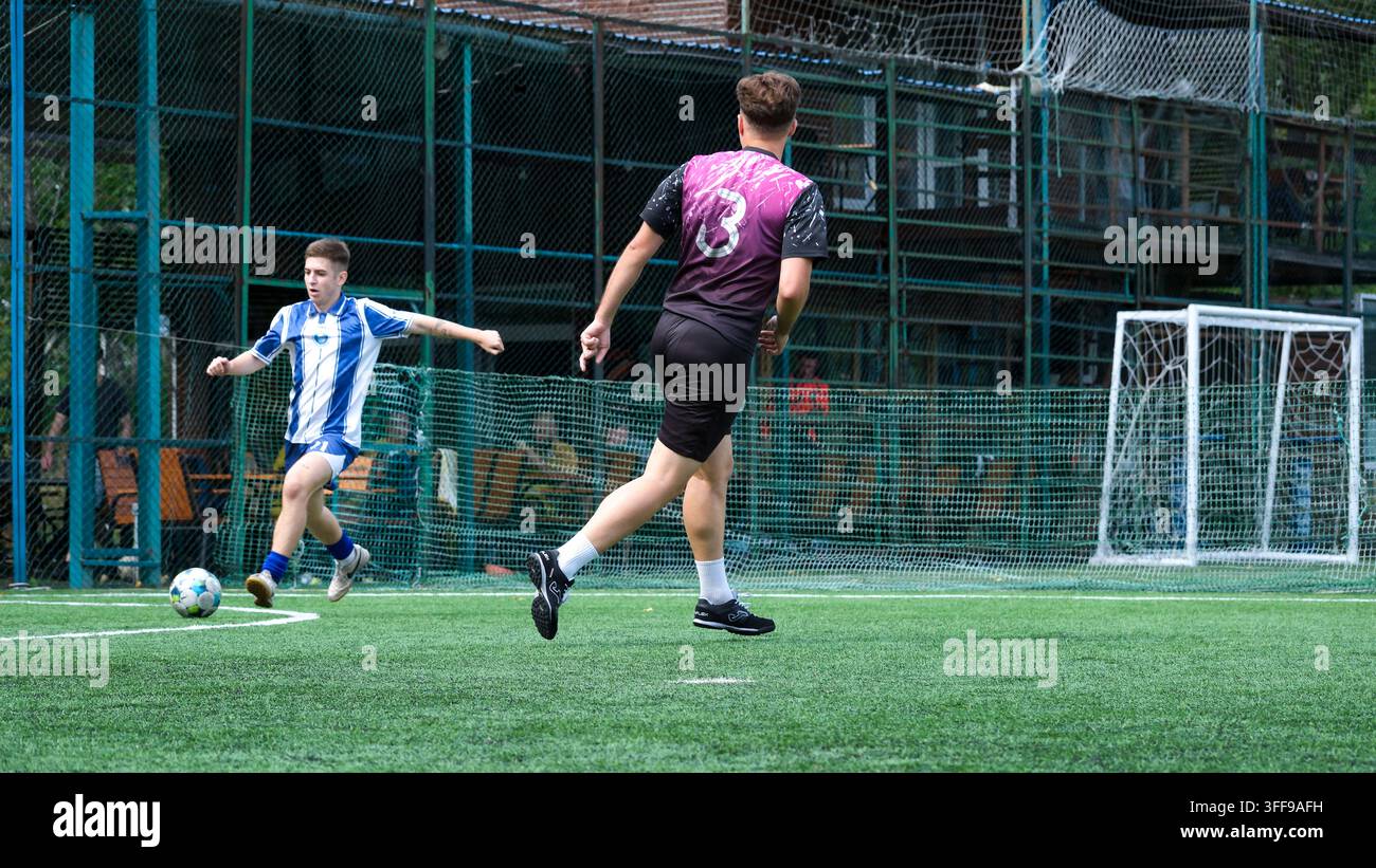 Joueur de football en uniforme bleu et blanc tire un coup alors qu'un adversaire défend pendant un match de football en plein air sur un terrain en gazon synthétique à Kyiv, U Banque D'Images