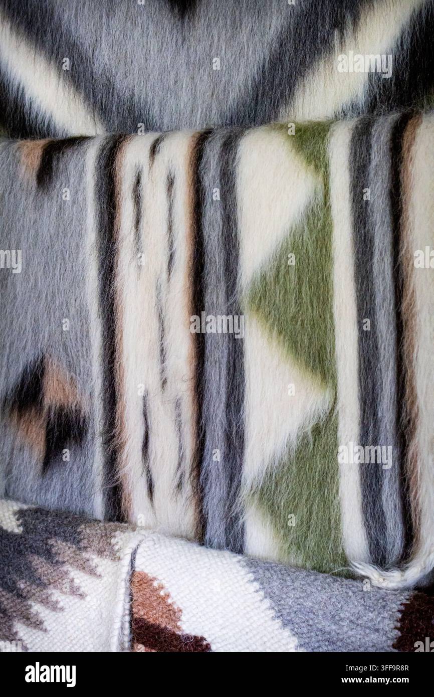 Des couvertures en laine douce avec des motifs géométriques empilées en couches montrent des tons subtils gris vert et terre. Les fibres tactiles et les motifs tribaux suggèrent une montagne Banque D'Images
