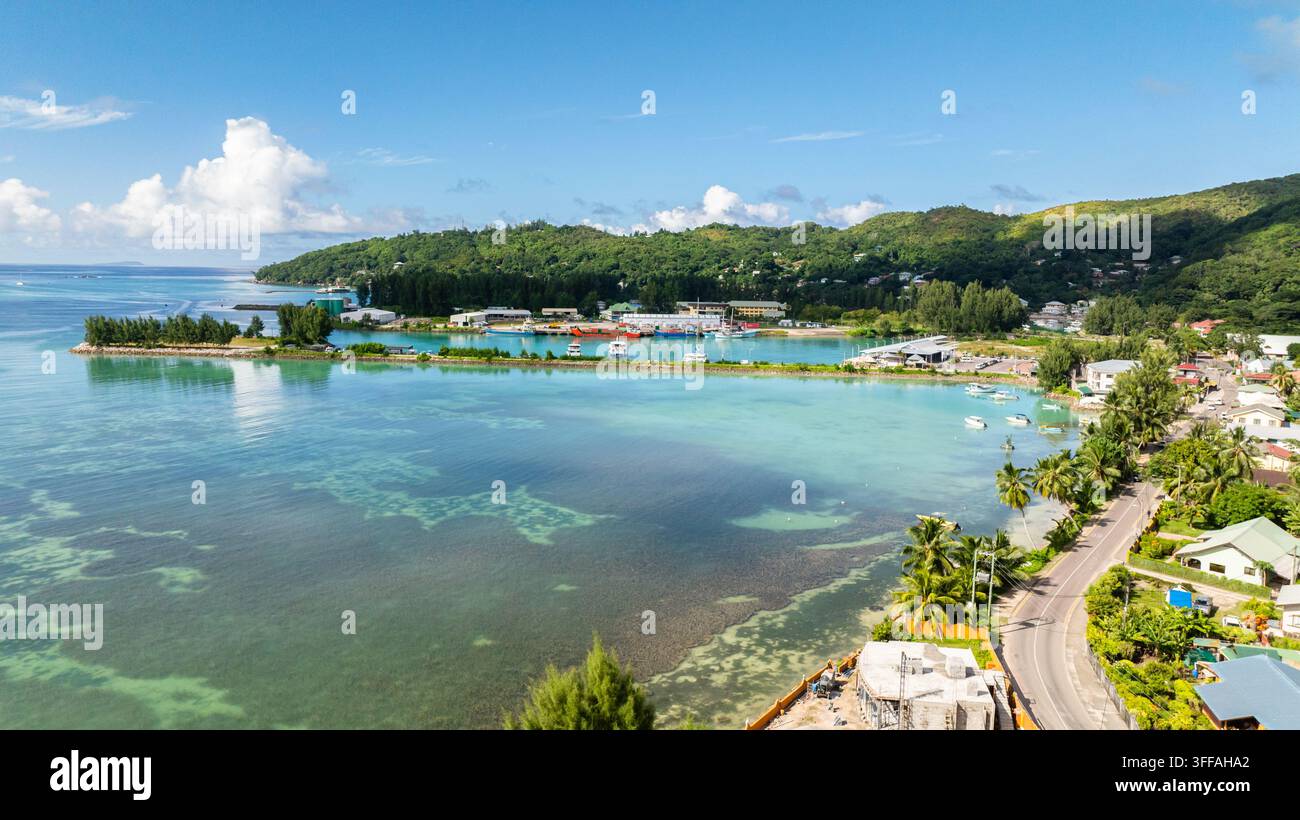 Une scène côtière avec des eaux turquoise, des bateaux amarrés et des collines vertes luxuriantes entourant une marina. Praslin, Seychelles. Banque D'Images