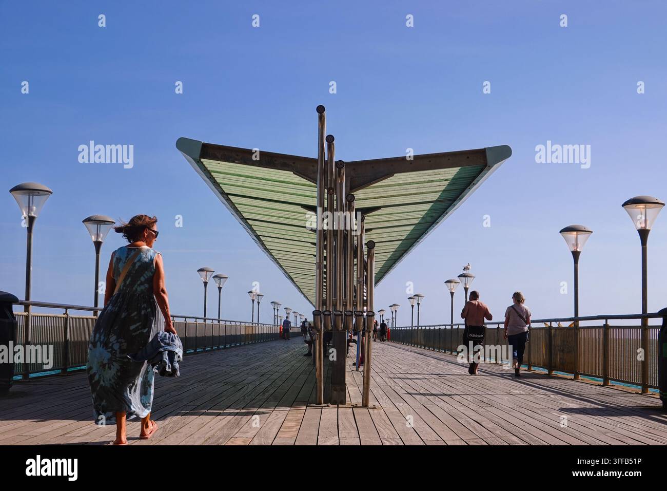 Des gens marchant le long de la passerelle en bois du Boscombe Pier à Bournemouth, Royaume-Uni, avec une structure de canopée moderne et la mer. Banque D'Images