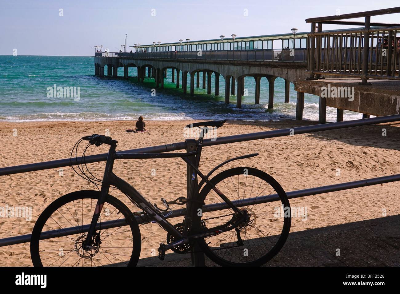 Un vélo attaché à une rambarde surplombant la plage de sable et le historique Boscombe Pier à Bournemouth, Dorset, Royaume-Uni. Banque D'Images