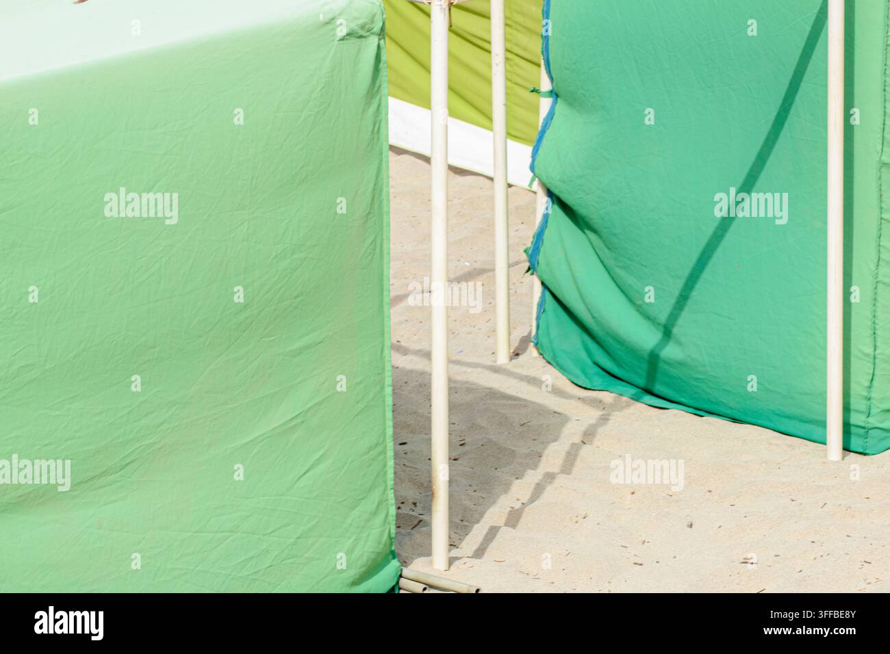Des poteaux en métal blanc soutenant une toile verte pour l'intimité et l'ombre sur une plage de sable Banque D'Images