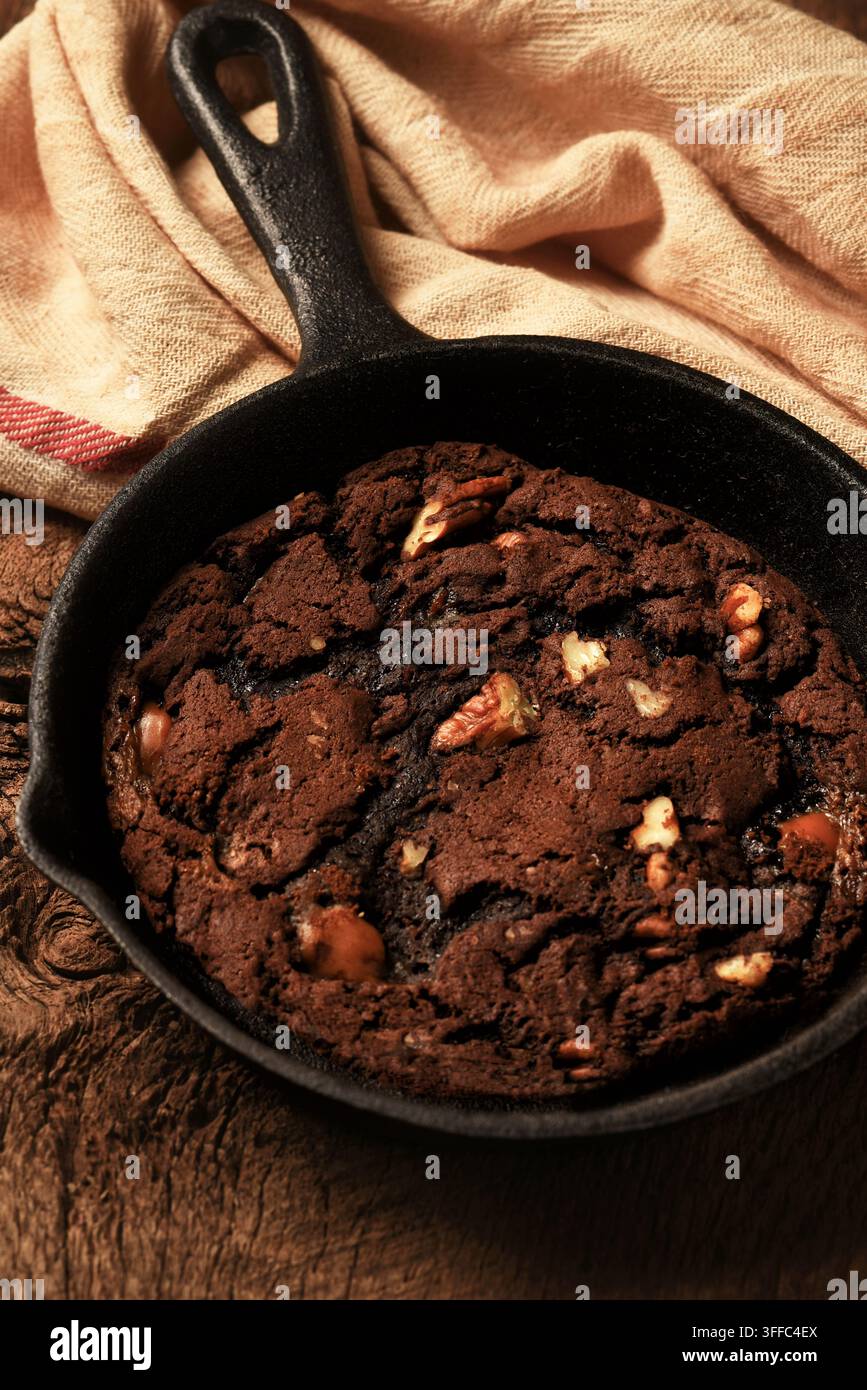 Nature morte avec un cookie brownie dans une poêle. Un cookie brownie aux pépites de chocolat et aux noix de pécan dans une poêle en fonte. Banque D'Images