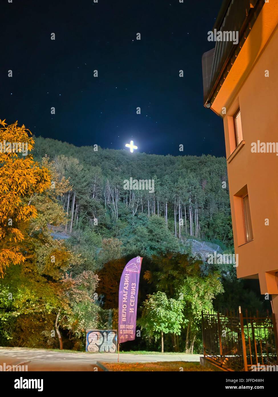 Croix chrétienne illuminée sur une colline boisée la nuit à Blagoevgrad, Bulgarie - Image de stock capturée avec un smartphone