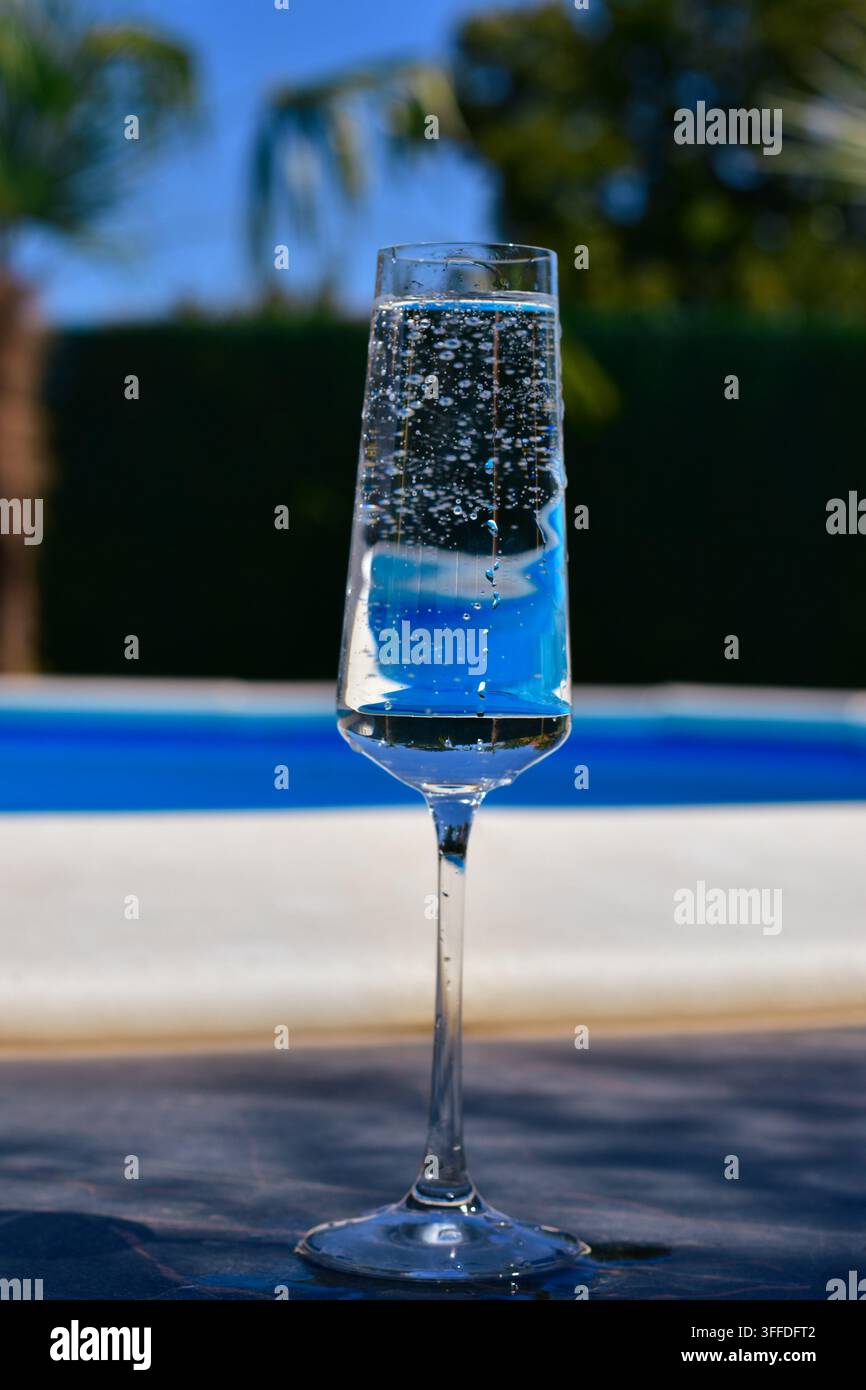 Verre à champagne avec de l'eau pétillante claire au bord de la piscine Banque D'Images