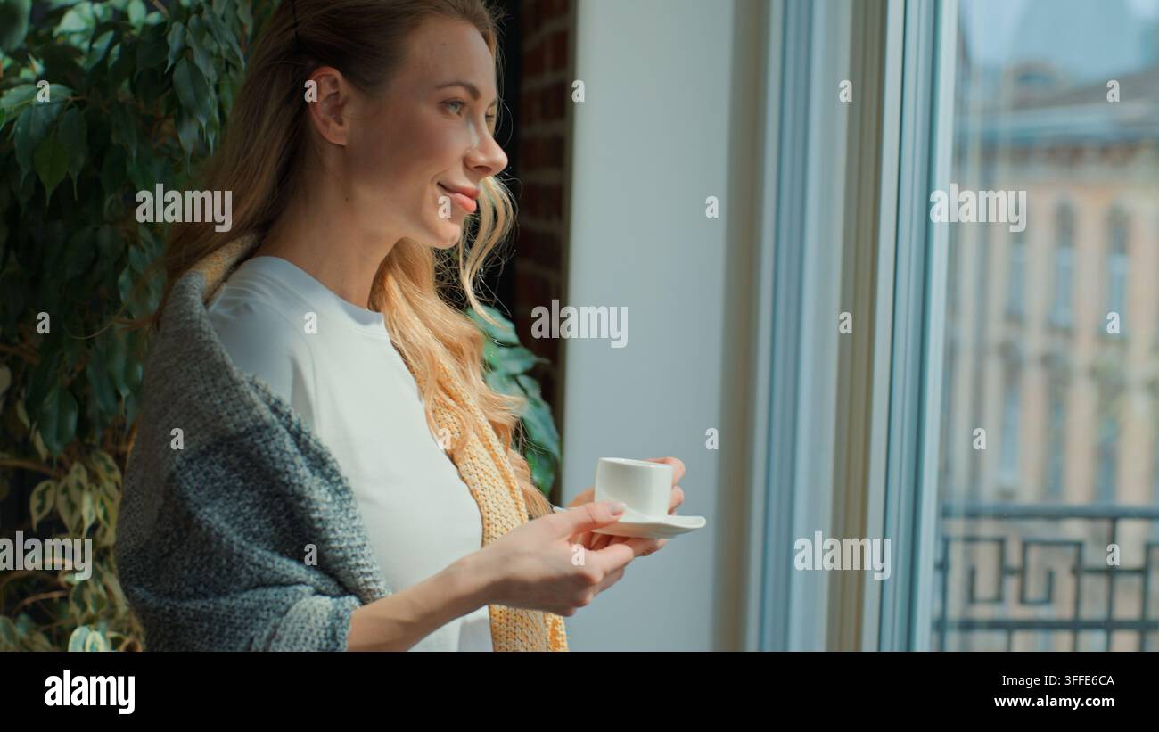 Femme caucasienne d'âge moyen calme buvant du café, inspirée, regardant par la fenêtre, profitant d'une pause matinale paisible à la maison, se détendant, adulte souriante Banque D'Images