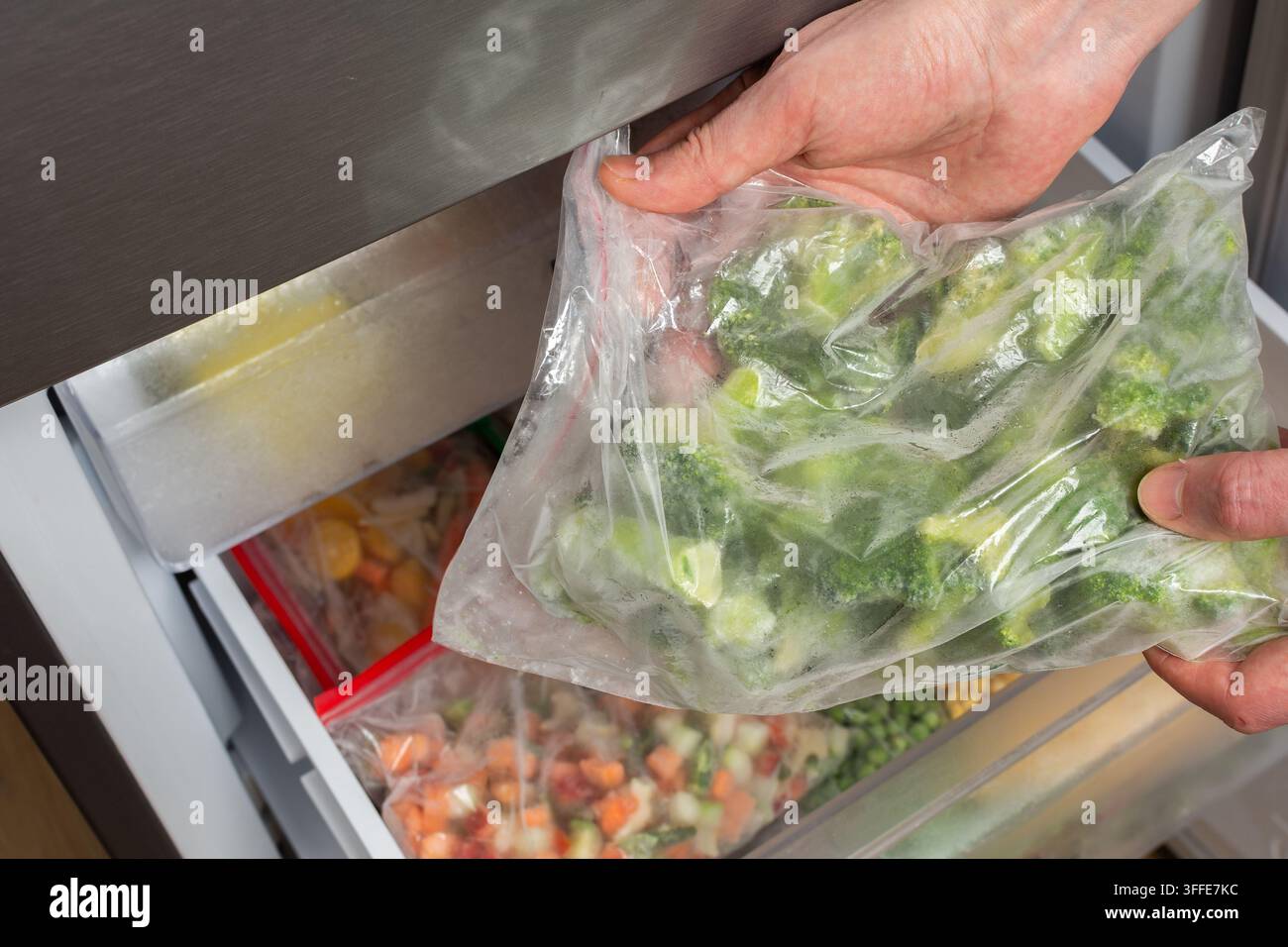 Un homme ouvre le réfrigérateur pour sortir un sac de brocoli surgelé. Il est dans la cuisine, préparant un repas pour le déjeuner. Le réfrigérateur Banque D'Images