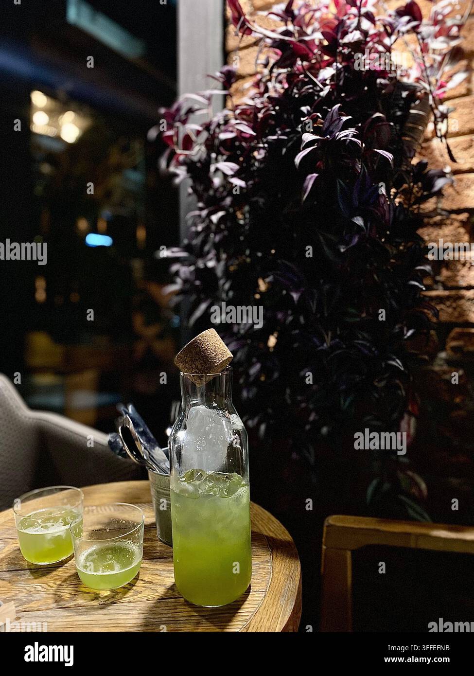 Boisson glacée verte servie dans une carafe en verre dans un restaurant doucement éclairé. - Image de stock capturée avec un smartphone