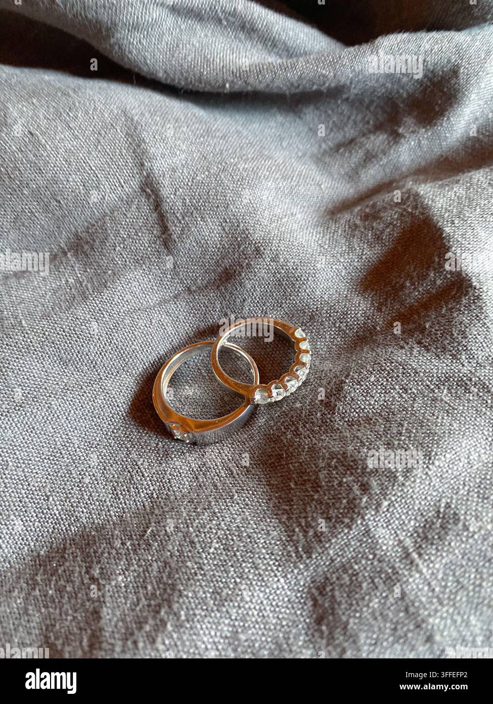 Deux anneaux en pierres précieuses reposent sur un tissu gris sous une lumière douce directionnelle. - Image de stock capturée avec un smartphone
