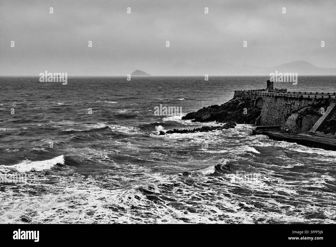 Mer Méditerranée agitée frappant un brise-lames historique en pierre sur la côte toscane, en Italie, avec des îles lointaines à l'horizon. Banque D'Images