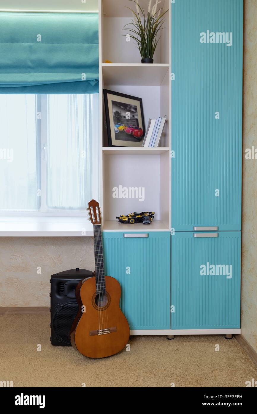 Guitare acoustique appuyée contre un meuble turquoise à côté d'une étagère de fenêtre avec des voitures miniatures, photographie encadrée Banque D'Images