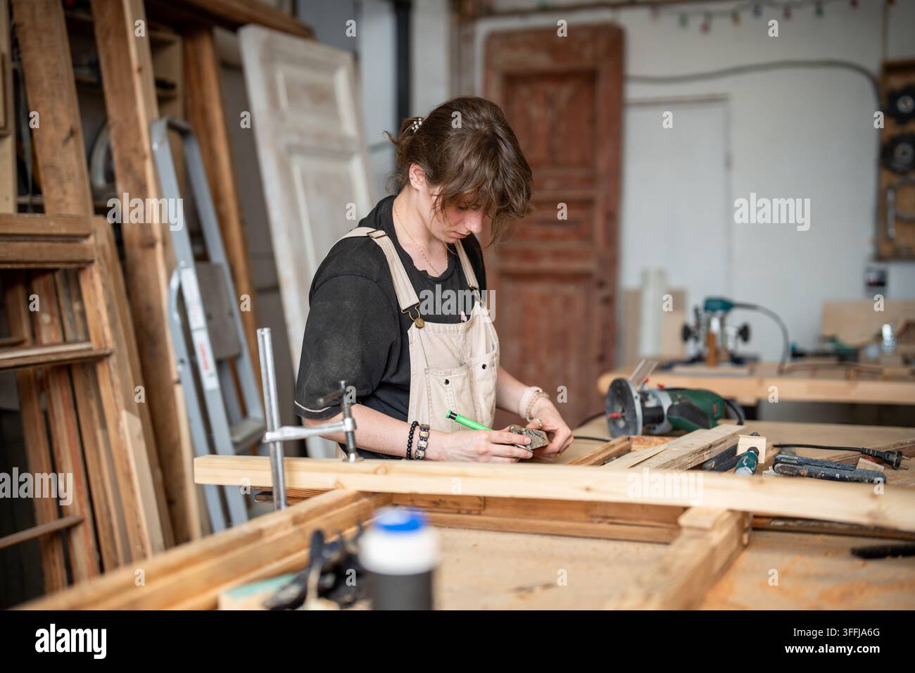 Restauratrice concentrée travaille dans un atelier de restauration sur un établi avec un cadre vintage et des instruments Banque D'Images