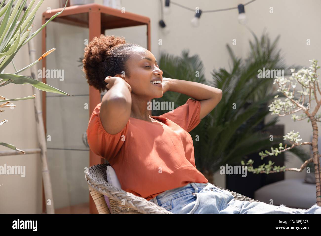 Femme se reposant à l'extérieur, assise confortablement dans une chaise en osier de jardin Banque D'Images