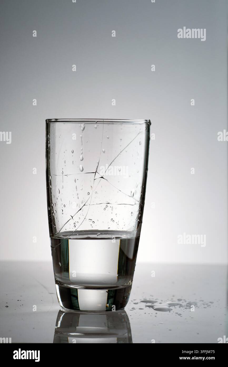 un verre brisé rempli d'eau avec de nombreux éclaboussures et gouttelettes sur la surface et la table en contre-jour Banque D'Images