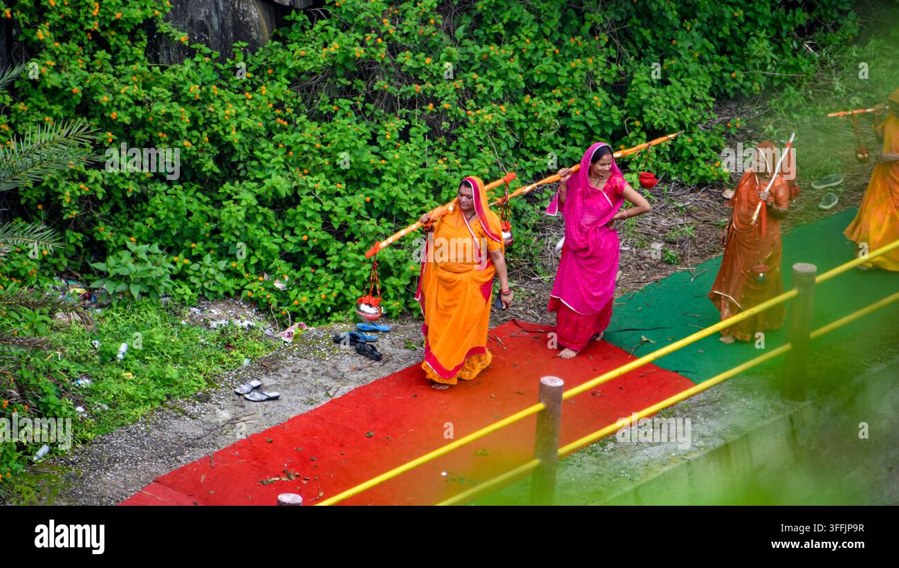 Des femmes indiennes portant un Kavad traditionnel sur leurs épaules lors d'un pèlerinage religieux, marchant dans une rue dans le cadre d'un voyage dévotionnel. Banque D'Images