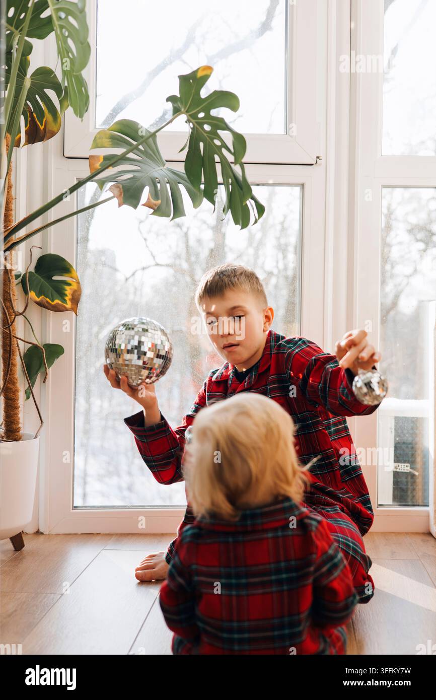 Deux frères en pyjamas à carreaux assortis jouant avec des décorations de Noël à la maison Banque D'Images