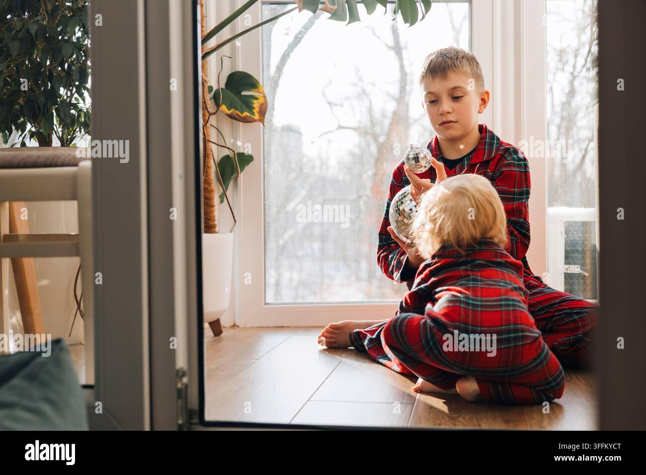 Deux frères en pyjamas à carreaux assortis jouant avec des décorations de Noël à la maison Banque D'Images