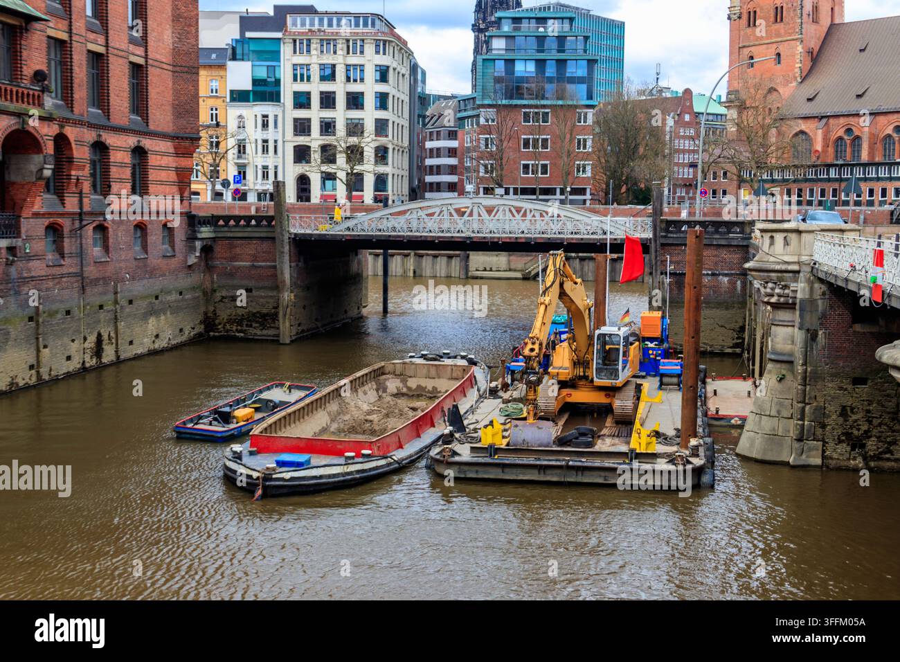 Excavatrice hydraulique jaune sur une péniche de construction effectuant des travaux de restauration à l'intérieur du canal du quartier historique de Speicherstadt à Hambourg, Ge Banque D'Images
