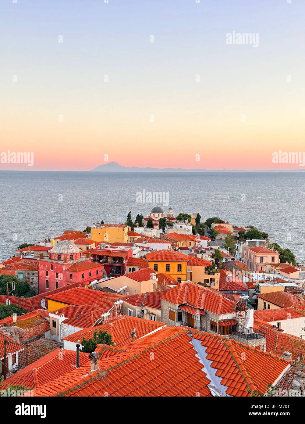 Vue panoramique en contre-plongée sur les toits en tuiles rouges de la vieille ville historique de Kavala, en Grèce, avec la mer Égée et la silhouette du mont Athos au coucher du soleil. - Image de stock capturée avec un smartphone
