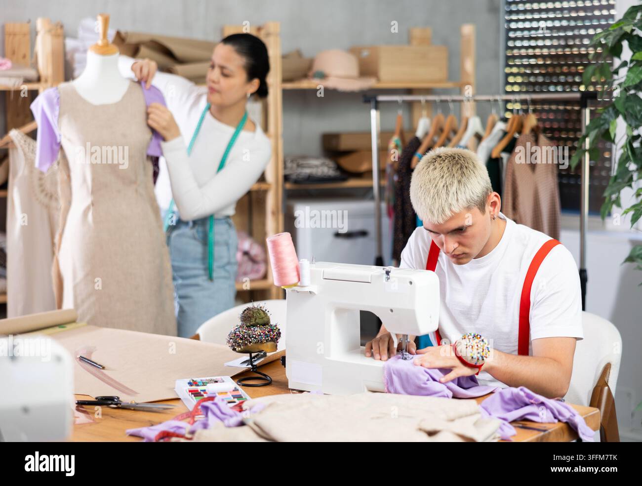 Une équipe de tailors travaille dans un atelier de couture pour coudre une collection de vêtements. Tailleur masculin cousant des vêtements devant le fond d'une femme asiatique travaillant Banque D'Images