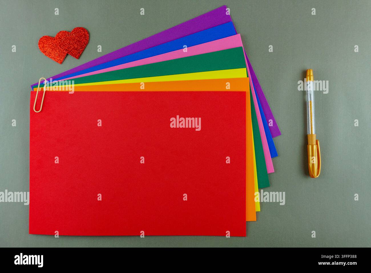 Vue de dessus d'un ensemble de papeterie lumineux avec une feuille rouge pour le texte, du papier couleur arc-en-ciel, deux cœurs pailletés et un stylo doré. Parfait pour la Saint-Valentin Banque D'Images