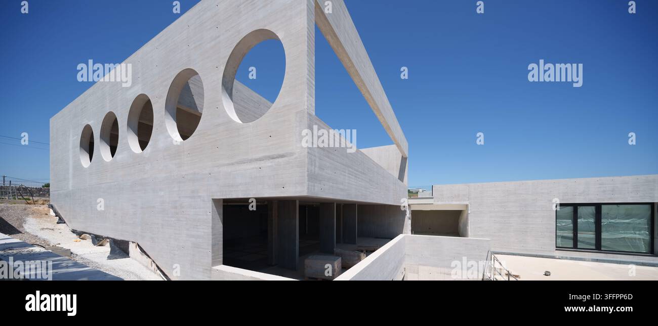 Hôtel contemporain en béton en construction présentant des ouvertures de fenêtres circulaires dramatiques, une architecture géométrique, une structure exposée et un bleu clair Banque D'Images