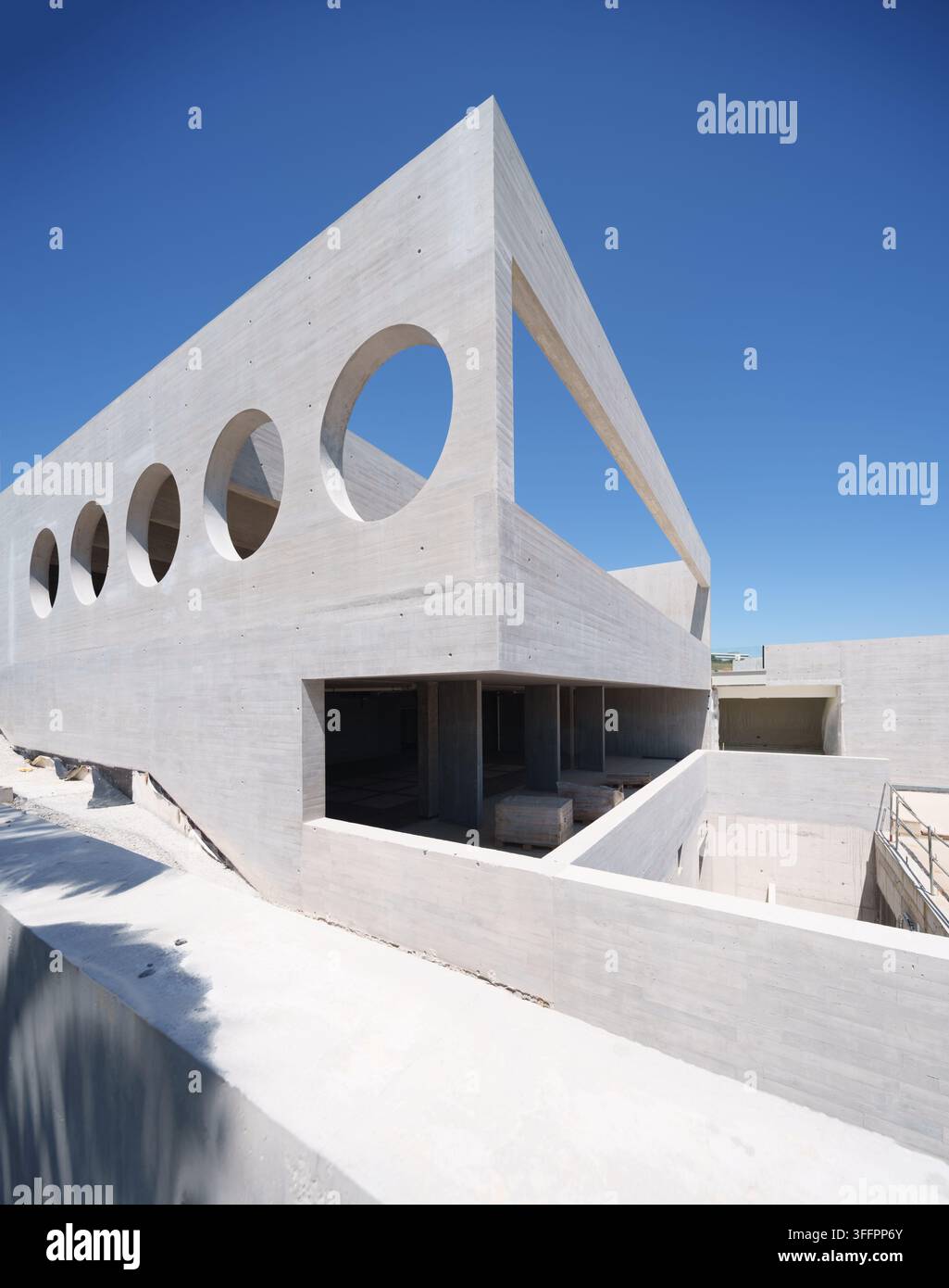 Bâtiment d'hôtel moderne en béton frappant en construction, présentant des ouvertures de fenêtres circulaires géométriques, des façades angulaires, des terrasses ouvertes et un bl clair Banque D'Images