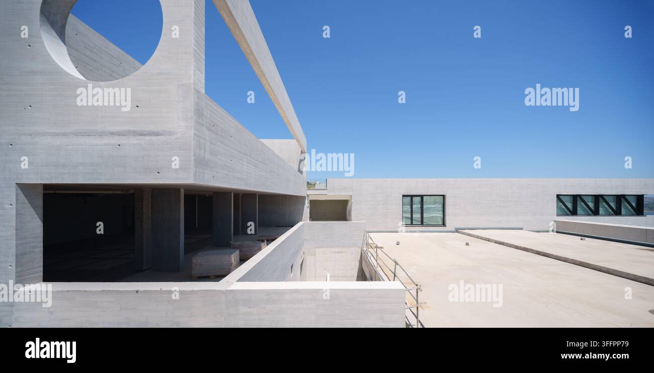 Hôtel contemporain en béton en construction avec des ouvertures géométriques, des terrasses plates sur le toit et une architecture minimaliste sous un ciel bleu clair à Banque D'Images