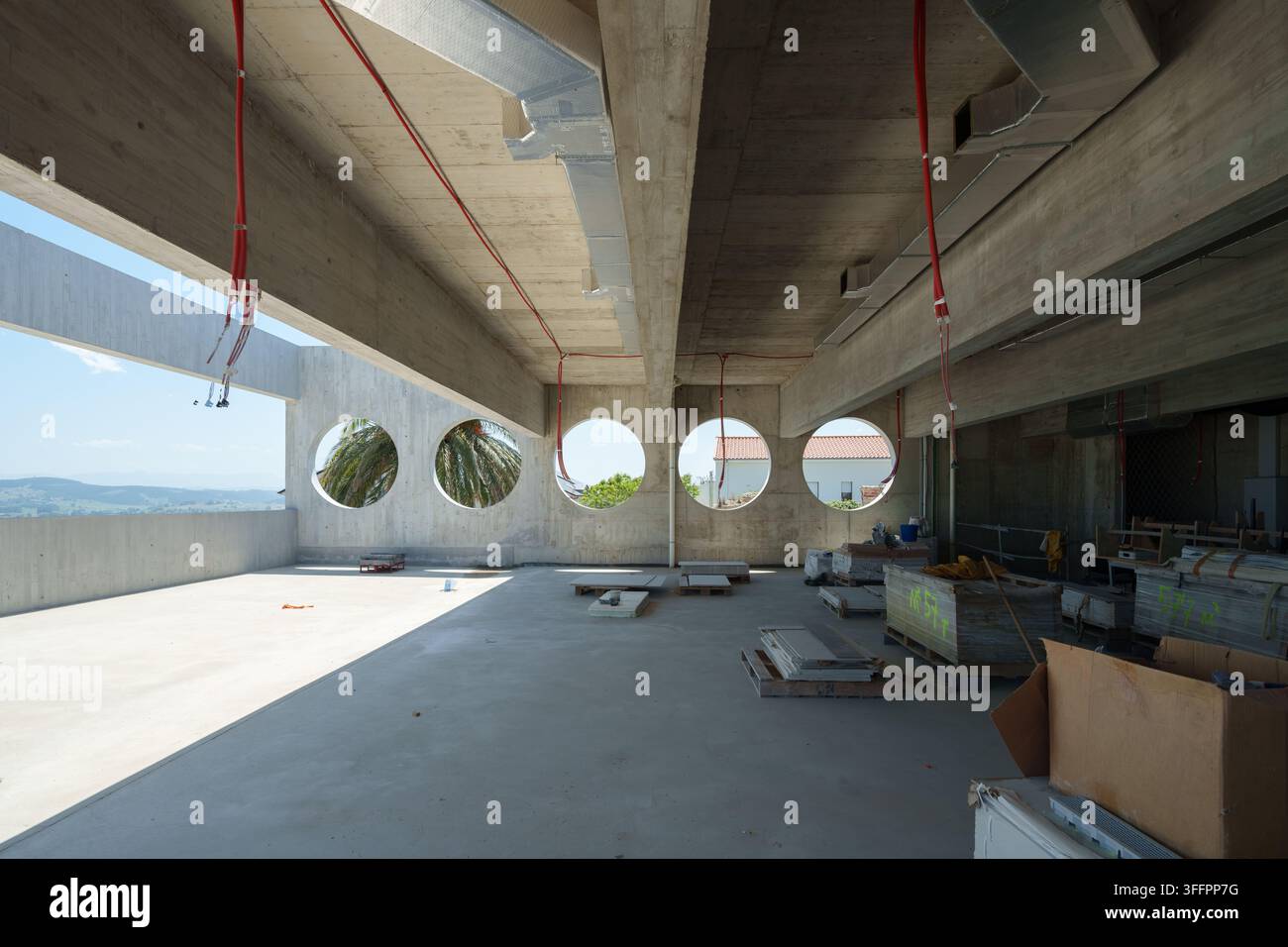 Vue large d'un intérieur d'hôtel en béton inachevé en construction, présentant des ouvertures de fenêtres circulaires, des plafonds exposés, des câbles suspendus, construction Banque D'Images