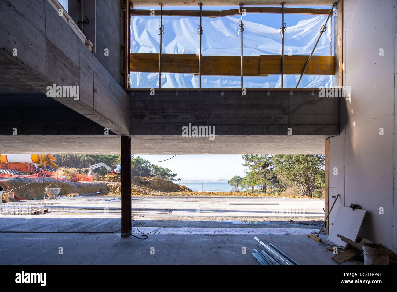 Vue intérieure d'un projet d'architecture en pierre en construction, avec béton apparent, charpente en bois et ouvertures recouvertes de plastique face à une côte Banque D'Images