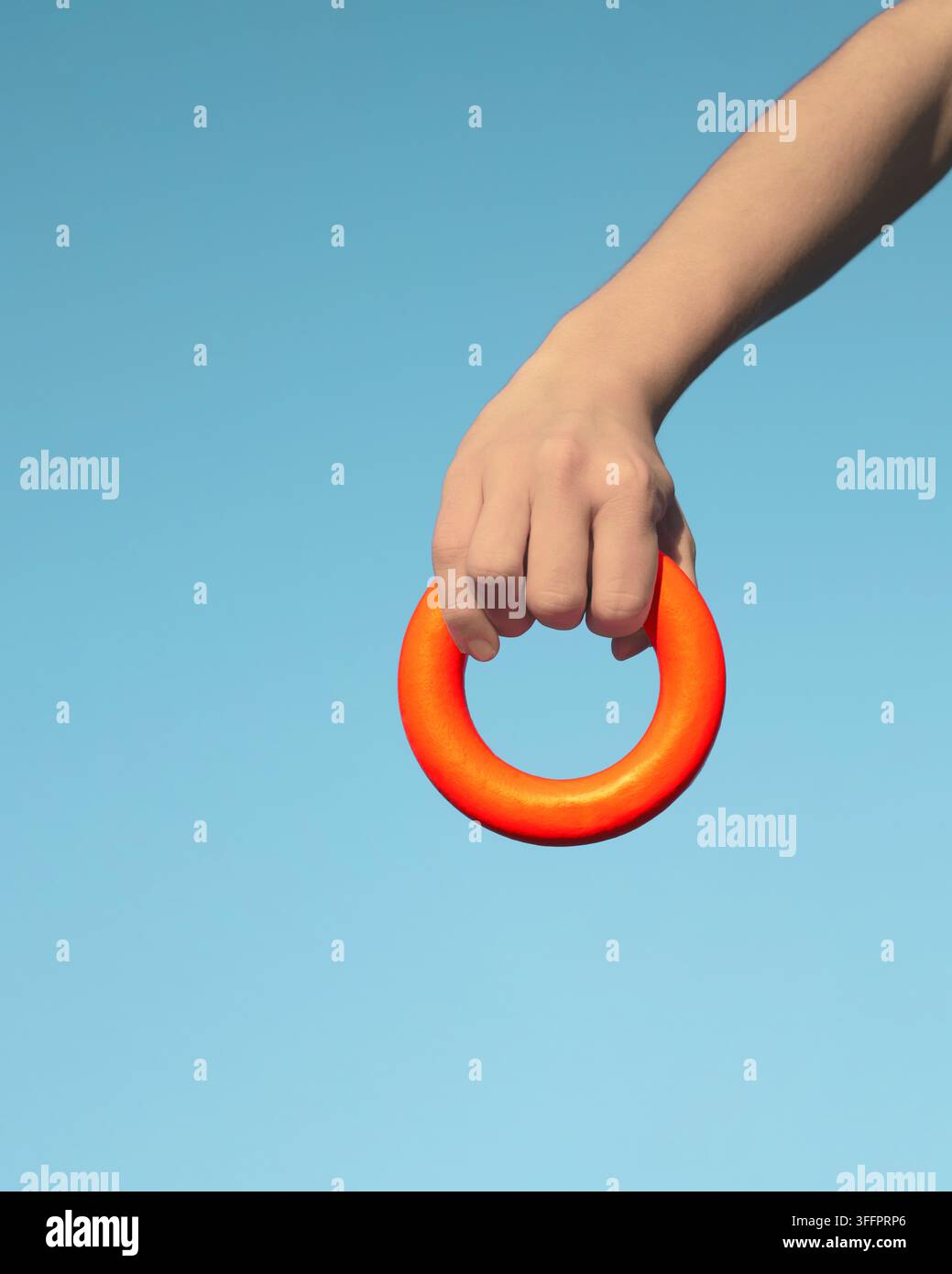 gros plan d'une main humaine tenant un anneau circulaire orange vif sur un fond bleu clair, créant une composition minimaliste avec des contrastes de couleurs audacieux Banque D'Images