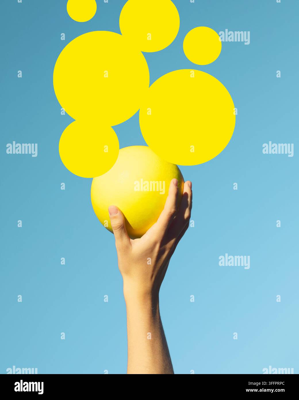 Une main humaine tient une sphère jaune lumineuse contre un ciel bleu clair, entourée de formes circulaires flottantes dans une composition médiatique surréaliste de co Banque D'Images