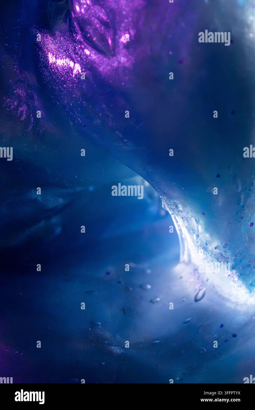 Texture liquide abstraite bleue et violette avec une vague lumineuse tourbillonnante, des gouttelettes suspendues et des nuages de pigments lumineux, créant un sous-marin cosmique Banque D'Images