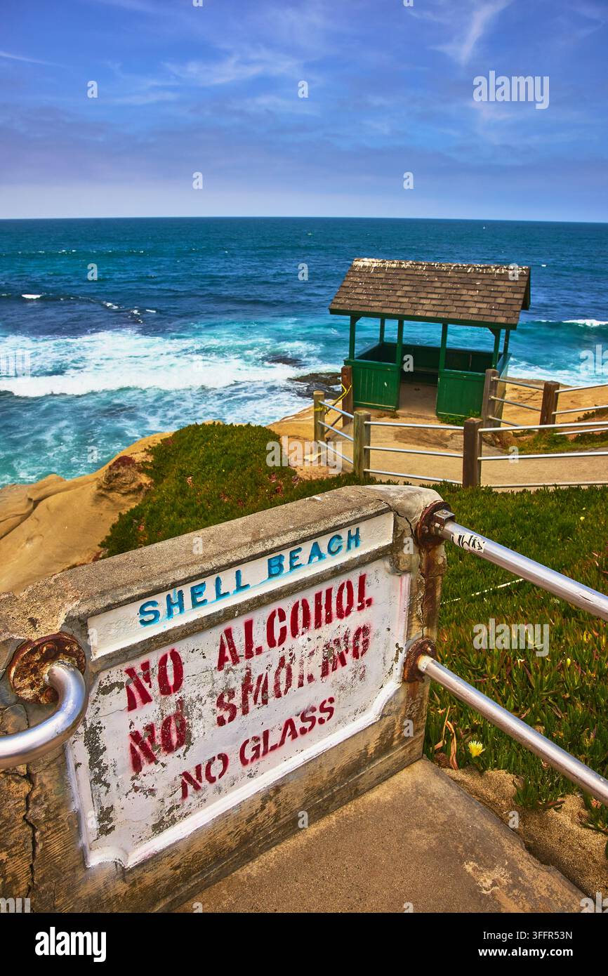 Un panneau usé de Shell Beach à La Jolla, en Californie, met en garde contre l'alcool, le tabagisme et les verres près de l'océan. L'abri côtier et les vagues d'un bleu éclatant Banque D'Images