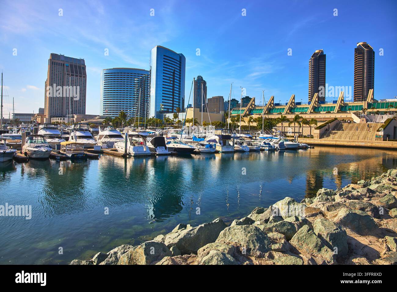 Des yachts élégants bordent le port de San Diego en Californie avec l’impressionnante skyline du centre-ville et le centre de conventions qui s’élève en arrière-plan. Ski lumineux Banque D'Images