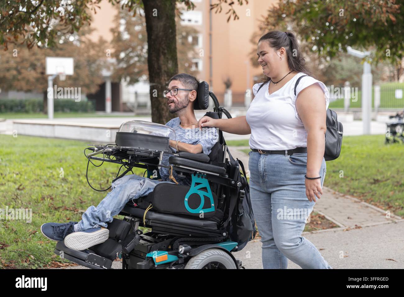 Assistante personnelle accompagnant un utilisateur de fauteuil roulant électrique lors d'une promenade paisible dans un parc herbeux en automne. Banque D'Images