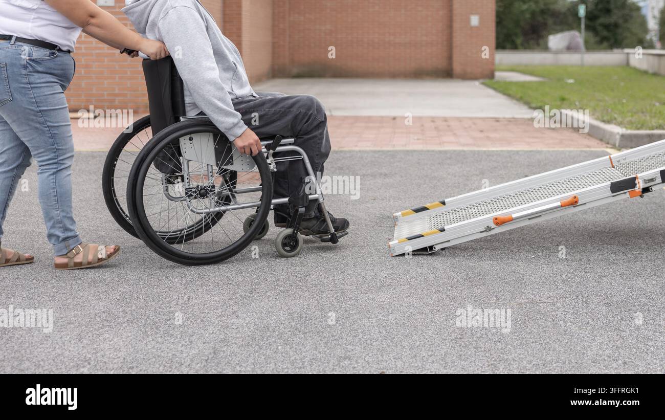 Utilisateur de fauteuil roulant profitant d'une promenade en plein air avec une assistante personnelle et utilisant une rampe pour voiture. Concept de soutien aux personnes handicapées et d'interaction sociale. Banque D'Images