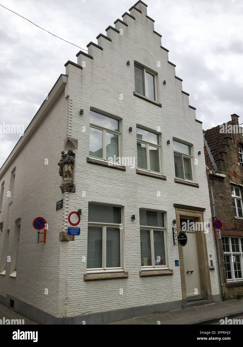 Une maison de ville en brique peinte en blanc avec un pignon en gradins et une petite statue d'angle située à un coin de rue à Bruges, en Belgique. Banque D'Images