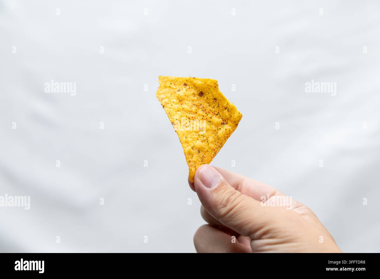 Main tenant une chipotle assaisonnée contre un fond clair, montrant une texture dorée et croustillante, une forme triangulaire et un espace de copie généreux. Banque D'Images