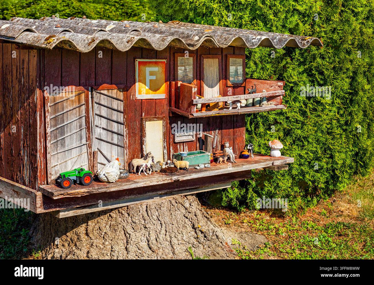 Charmante ferme suisse miniature en bois construite sur une souche d'arbre avec des animaux jouets et un tracteur vert Banque D'Images