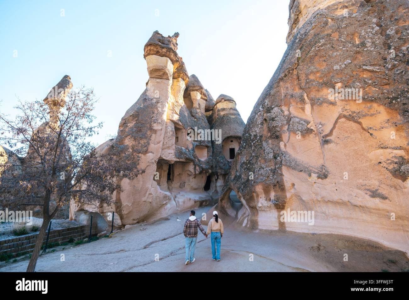 Deux personnes se promènent main dans la main à travers le paysage enchanteur de la Cappadoce, émerveillées par les magnifiques cheminées de fées qui s'élèvent au-dessus d'elles. Le soleil c Banque D'Images